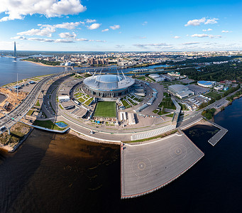 飞行中的直升机摄影照片_俄罗斯，圣彼得堡，2020 年 9 月 1 日：无人机视角的新体育场 Gazprom Arena，2020 年欧洲杯，可伸缩足球场，背景中的摩天大楼 Lakhta 中心，晴朗的天气，直升机停机坪