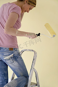 长梯子摄影照片_带油漆滚筒的梯子上的女人