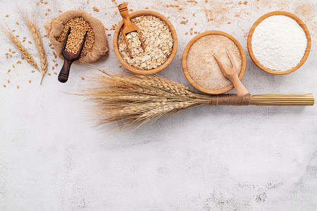 在白色混凝土背景下设置的木碗中的小麦籽粒、棕色小麦面粉和白色小麦面粉。