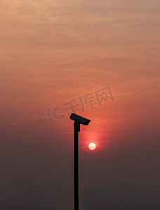前景中的现代监控摄像机 橙色的太阳在太阳落山前闪耀。