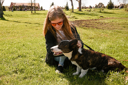 戴着红色太阳镜的年轻女人在夏日的绿色草坪上和她的柯基犬玩耍