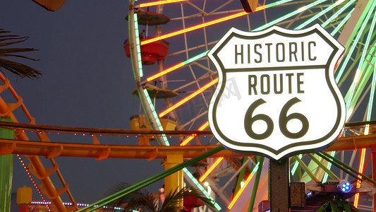 路线卡摄影照片_美国洛杉矶圣塔莫尼卡 — 2019 年 10 月 28 日：标志性路标发光，历史悠久的 66 号公路。著名的加利福尼亚标志，太平洋度假村码头。