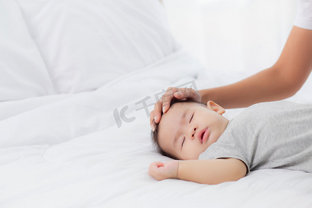 小女摄影照片_年轻的亚洲母亲抚摸着卧室床上柔软的小女婴的头，妈妈爱新生儿和照顾，与孩子一起表达的女人，父母和女儿，家庭观念。