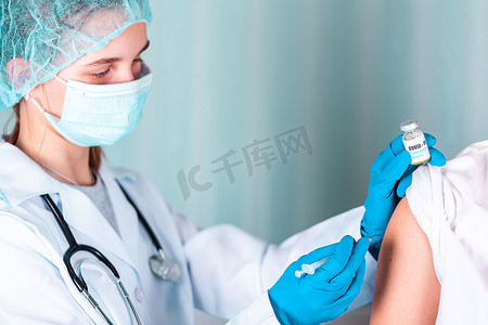 身着制服和手套的医生或护士在实验室制作带有 COVID-19 冠状病毒疫苗标签的注射疫苗瓶