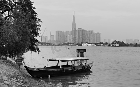 2019-11-10 / 越南胡志明市 - 一个穷人将船推入河中，背景是高大的现代摩天大楼。
