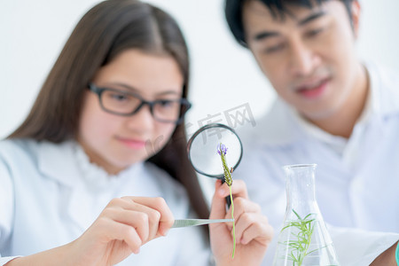 花由年轻的白人科学家女童拿着，通过放大镜看，向导也支持亚洲老师在课堂实验室。