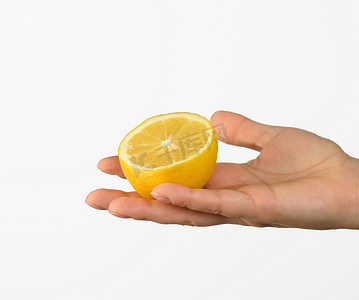 半握的手摄影照片_白色背景中，女手握着半个黄色柠檬