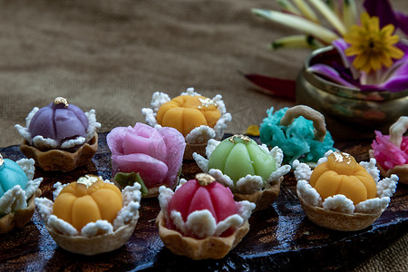吉祥麒麟摄影照片_各种优雅美丽的泰式甜点 (Khanom Wan Thai) 五颜六色的变化在深色木头中供应，金色和不同花朵形状的叮咬，泰式甜点，吉祥甜点。