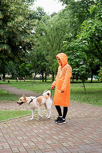 穿着橙色雨衣的年轻女子和她的狗在公园里散步