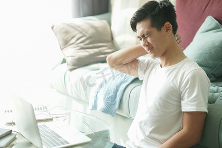 疲惫不堪、沮丧的亚洲学生男性青少年企业家在家工作时颈部疼痛