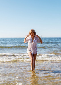 身穿湿白衬衫的年轻金发女子从海边附近的水里出来