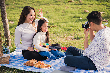 一家人的父亲、母亲和孩子一起玩乐，享受户外活动，坐在草地派对上拍照