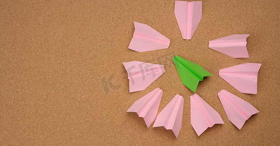 纸飞机粉色摄影照片_绿色纸飞机被棕色背景中的粉色纸飞机围成一圈