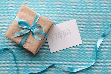 包裹丝带摄影照片_用牛皮纸包裹的礼品盒，蓝色背景带丝带，带贺卡。