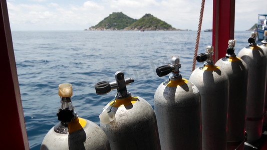 在泰国涛岛度假村附近波涛汹涌的海洋中，一排氧气罐和潜水设备被放置在现代船上。