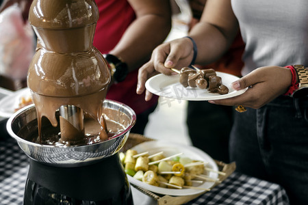 自助餐桌上有水果串的巧克力喷泉餐饮机