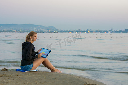 坐在沙滩上用日落画风景的小女孩