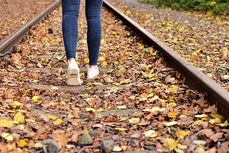秋叶上穿蓝色牛仔裤和白鞋的步行腿