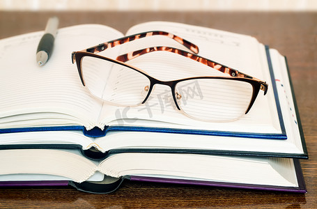 阅读桌摄影照片_桌面上的眼镜、书籍和笔记本。