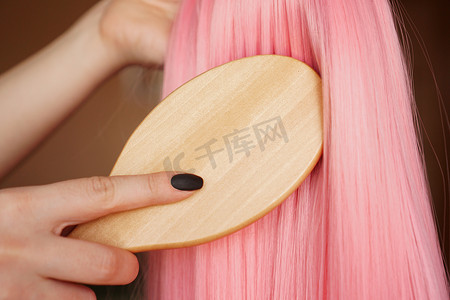女手拿着长发粉色假发，梳着木梳