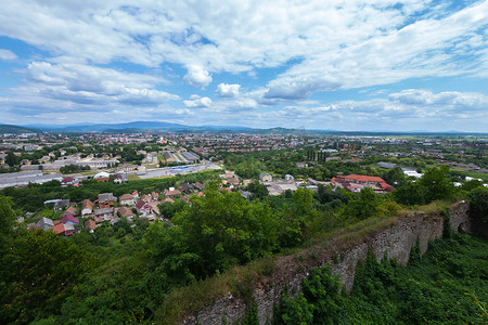 从一座长满灌木和草的古堡倒塌的围墙后面可以看到现代城市的屋顶和