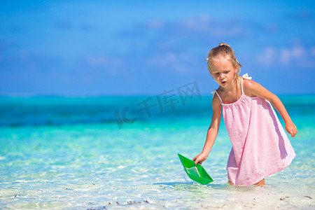 小纸船摄影照片_在绿松石海中玩纸船的可爱小女孩