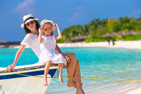 家庭度假摄影照片_海滩度假期间在船上的小女孩和年轻母亲