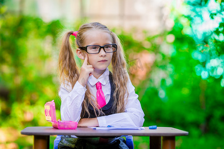 聪明的小女生坐在办公桌前，带着笔记和铅笔在户外。