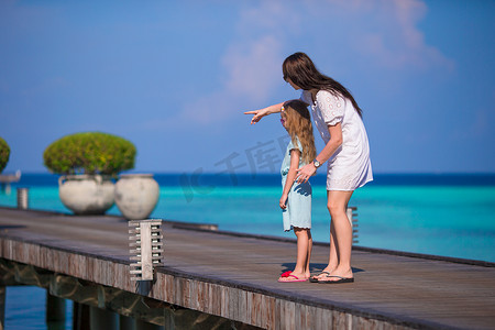 家庭度假摄影照片_在异国情调的度假胜地的木码头上行走的小女孩和年轻母亲