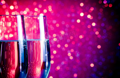 紫色气泡饮料摄影照片_蓝色和紫色浅散景背景上带有金色气泡的香槟长笛