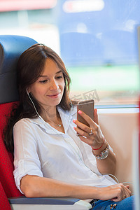 坐火车旅行摄影照片_年轻快乐的女孩听音乐，读乘火车旅行的信息