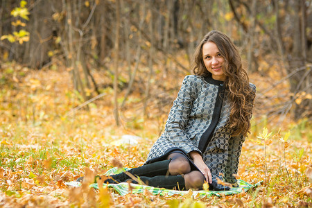 一件黄色外套的年轻美丽的女孩坐在森林里的落叶上