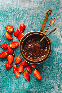 草莓味糖果摄影照片_在铜锅和旁边的草莓片中融化黑巧克力。