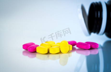 黄色和粉红色的椭圆形药丸，白色背景上有阴影，药瓶模糊。