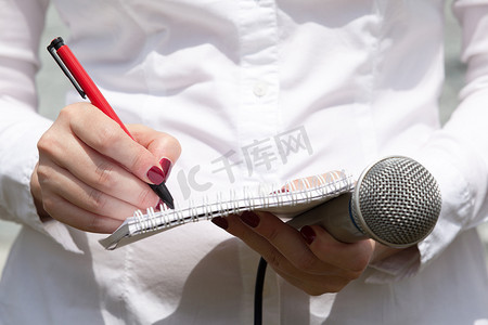 新闻新闻摄影照片_新闻发布会上的女记者，写笔记，拿着麦克风