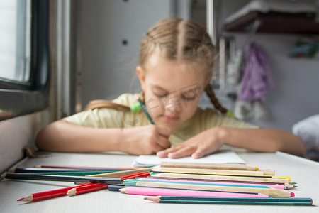 前景中的铅笔，背景中一个六岁的女孩在二等火车车厢里画铅笔