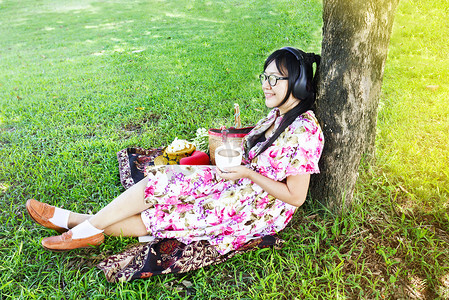 室外音乐摄影照片_戴墨镜的亚洲年轻女性开心地笑着听音乐