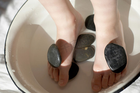 洗脚摄影照片_孩子的脚在带石头的洗脸盆里