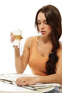 坐在桌边看报纸、拿着拿铁玛奇朵咖啡的年轻女人