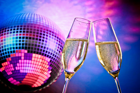紫色气泡饮料摄影照片_一对带有金色气泡的香槟长笛在闪闪发光的蓝色和紫色迪斯科舞会背景上欢呼