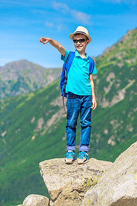 男孩旅行者站在岩石上，出现在一座山上
