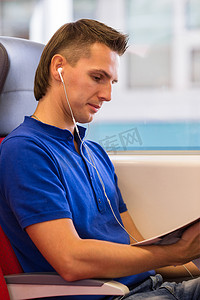 坐火车旅行摄影照片_坐火车旅行的年轻快乐男人听音乐
