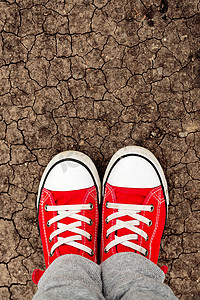 鞋子男孩摄影照片_站立在地面上的红色运动鞋的男孩，从上面