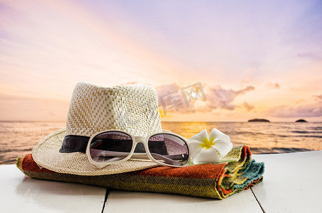 帽子、眼镜、围巾、鲜花放在以大海为背景的木地板上。