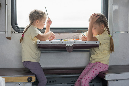 两个女孩为二等火车车厢的边桌画画