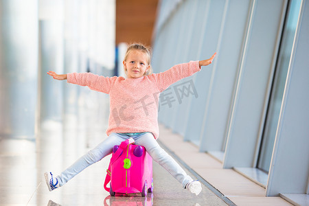 坐在手提箱上在机场玩得开心的可爱小女孩