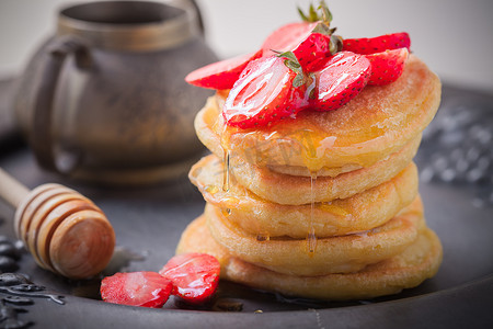 薄烤饼摄影照片_堆栈的甜薄煎饼用草莓和蜂蜜。