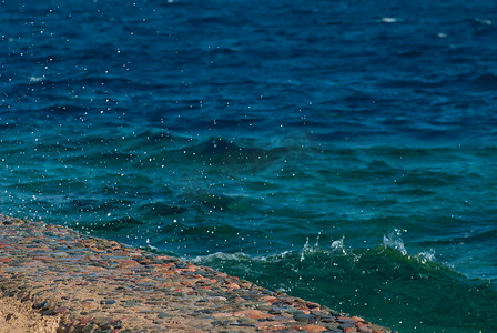 有波纹摄影照片_美丽清澈的绿松石海水面照片，石质海景背景上有波纹和明亮的飞溅，水平图片