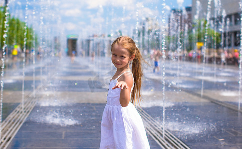 阳光明媚的炎热日子里，快乐的小女孩在街头喷泉里玩得开心