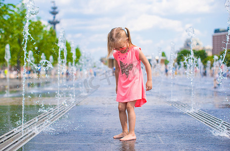 炎热公园摄影照片_小女孩在炎热的阳光明媚的日子里在露天喷泉里玩耍